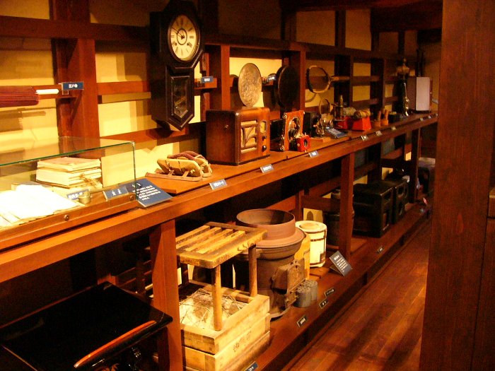 長机のある部屋に時計や生活用品など様々な展示物が並んでいる写真 拡大画像