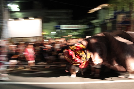 温泉街の道路を行く大きな獅子舞いとそれを沿道で見る人々の写真