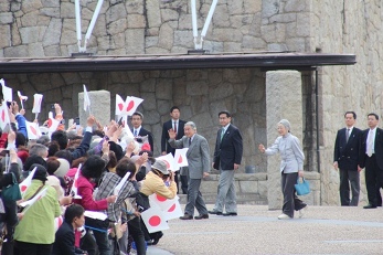 日の丸の旗を持った人たちが両陛下の見学を歓迎している写真