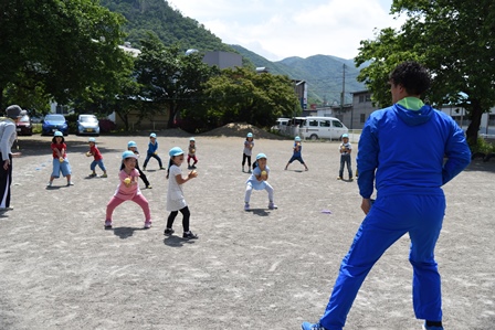 投球ポーズの練習をする園児達と、指導する田中健太郎さんの写真