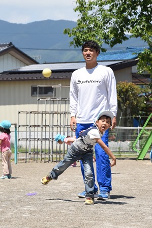 ボールを投げる少年と、それを背後から見守る田中健太郎さんの写真