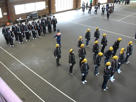 屋内テニスコートで整列する新入団員や黄色い帽子を被った婦人消防隊員達の写真