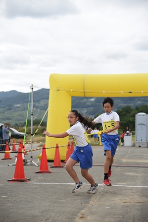 駅伝を走る小学生の男の子が小学生の女の子の選手にタスキを渡す瞬間の写真