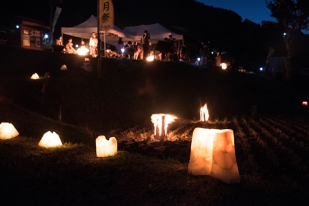 キャンドルが手前に大きく映り、奥に夜の祭りの様子がうつる夜景の写真