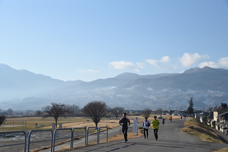 堤防道路を走る市民ランナーとその後ろに山々の景色の見える写真