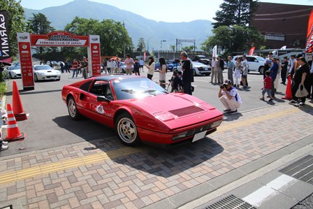 イベント会場で赤いフェラーリを眺めている人達の写真