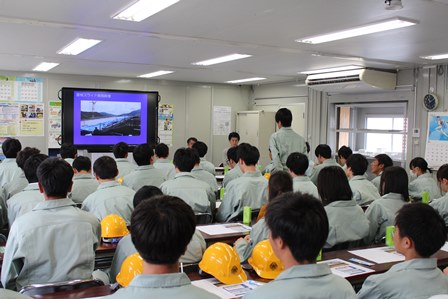 つなぎを着た高校生41人が机に座ってスクリーンの資料を見ている写真