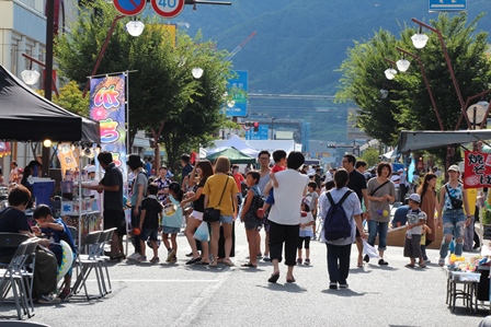 道路に出店が並ぶ夏祭りの昼間の写真