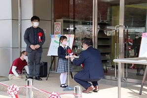 交流センターの玄関先で市長と女の子が作品の受け渡しをしている写真