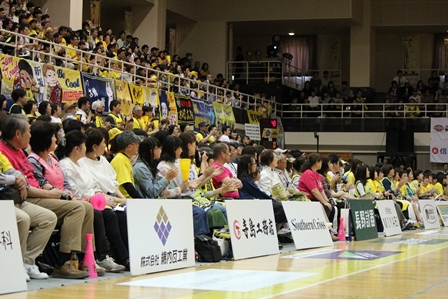 コートラインの外側の席に座りバスケットボールの試合を観戦する観客たちの写真