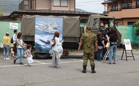 ポスターが張られた自衛隊のトラックと自衛隊員と見学している人たちの写真