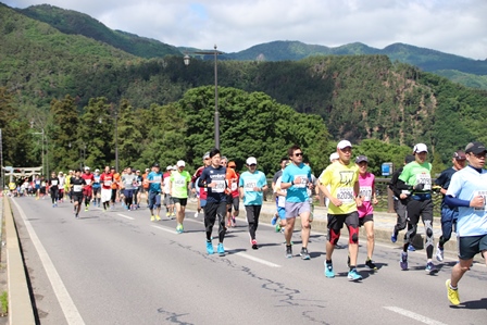 山が見える道路を大勢のマラソンランナーが走っている写真