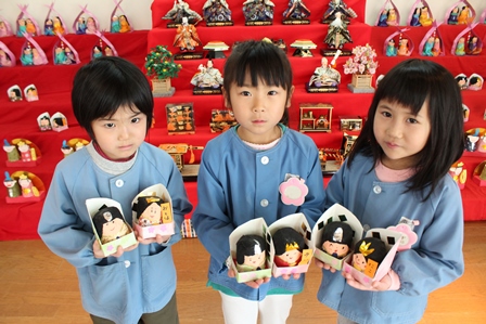 雛壇の前で手作りの雛人形を持った園児3人の写真