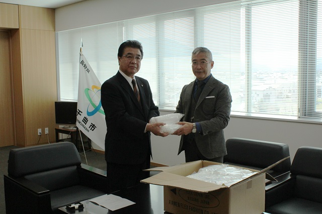 市長と矢島さんがカメラのほうを向きながら寄贈品の受け渡しをしている写真