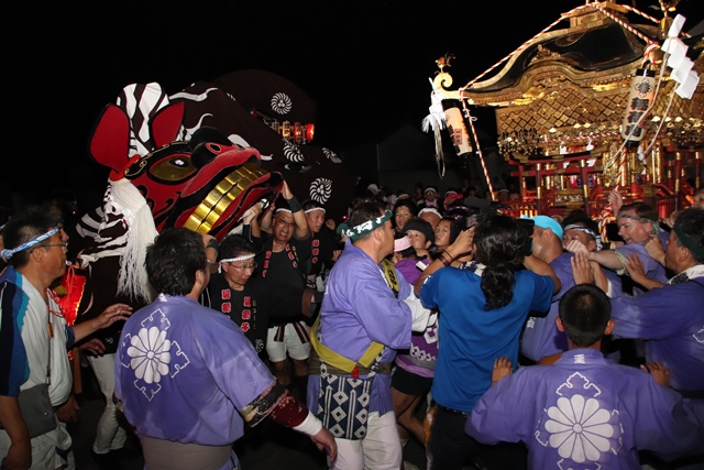 大勢の人と獅子舞と神輿が対面している夏祭りの夜の写真