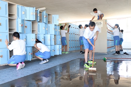 デッキブラシなどを使いロッカーと共有スペースの掃除をしている生徒たちの写真