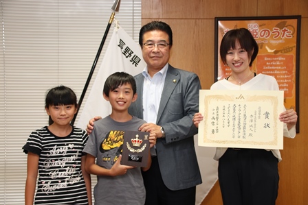 コンクールで最優秀賞に選ばれた男の子と家族が賞状を持って市長と一緒に並んでいる写真
