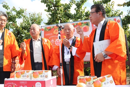 市長と生産者がオレンジ色の半被を着てあんずを試食している写真
