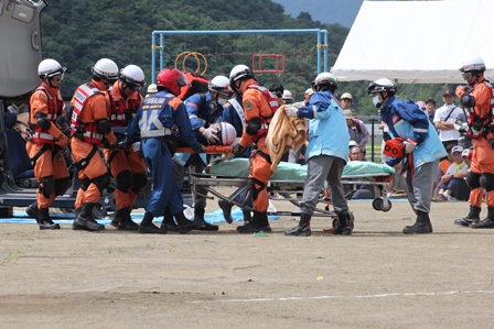消防団員と救急隊員が負傷者を運び担架に乗せる訓練をしている写真