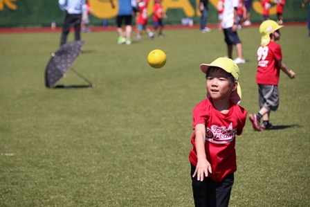 芝生の上でボールを投げてる赤いTシャツの男の子の写真