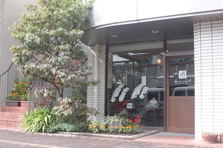 建物の一階の一角にある植木花と花壇があるカフェの外観の写真