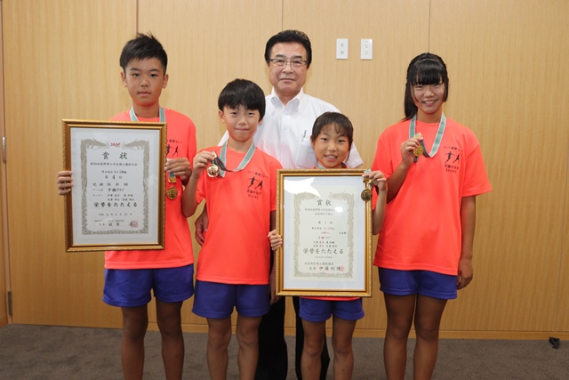 オレンジ色のユニフォームを着て表彰状やメダルを持ち記念撮影をする児童らの写真