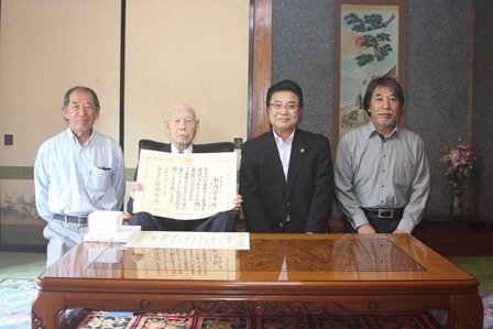 おじいさんが100歳を迎えた賞状を持ち和室で市長と家族と一緒の写真