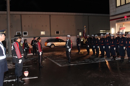 夜の消防署前で消防団員から人員報告を受ける副団長達と、整列している消防団員達