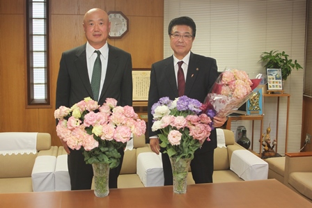 花瓶を2つ手前に男性と市長が花束を手にしている写真