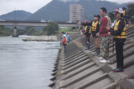千曲川の河川敷で並んで釣りをしている子供と大人数名の写真