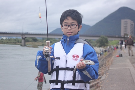 釣り竿と釣ったニジマスを手に持った眼鏡の男の子の写真