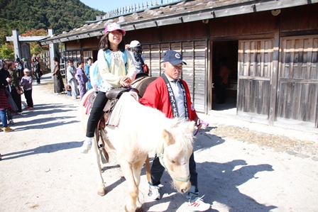 小屋の近くで乗馬体験をする女の子と付き添っているおじいさんの写真