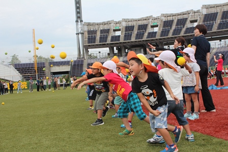 園児たちが元気よくスタジアムでボール投げをしている写真