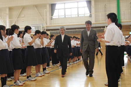 体育館内に集まった生徒たちに拍手で迎えられる倉島さんの写真