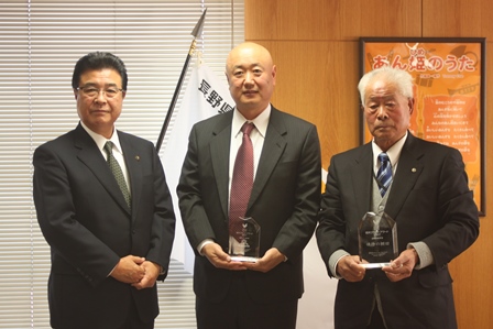 透明なオブジェを手に、岡田市長と並んで立つ中曽根健さんと佐藤基さんの記念写真