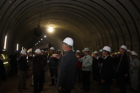 トンネルの貫通をヘルメットを被った50人が見守っている写真