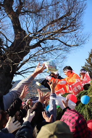 祭りに集まった人たちがトラックからまかれた小袋にむかって手を伸ばしている写真