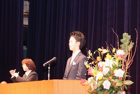 成人式のステージ上で誓いをのべる新成人男性と隣で手話通訳をする女性の写真