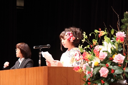 成人式のステージ上で誓いをのべる新成人女性と隣で手話通訳をする女性の写真