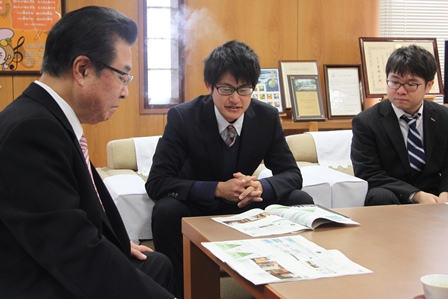 市長室で市長と資料を見つめる男子大学生二人の写真