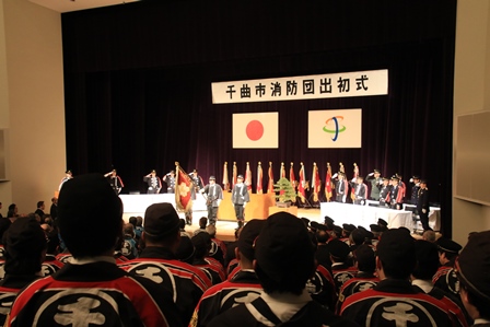 会館で行われた消防団の出初式で団員が集まってステージ上の式を見ている写真