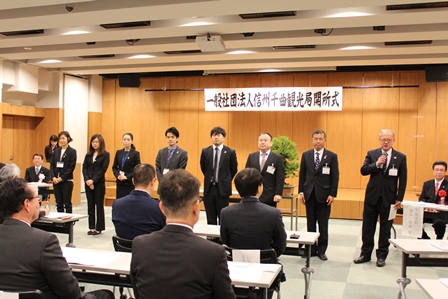 室内の開所式で数名のスタッフが前に立ち、代表者が参加者の前でスピーチしている写真