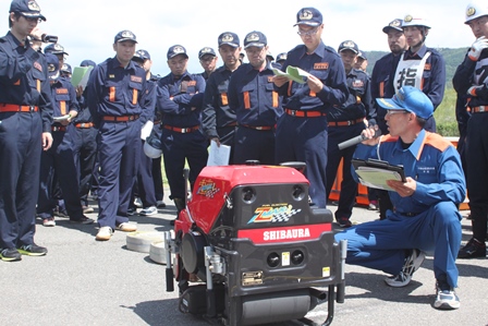 訓練で消防職員からポンプの機械の説明を受ける消防団員の写真