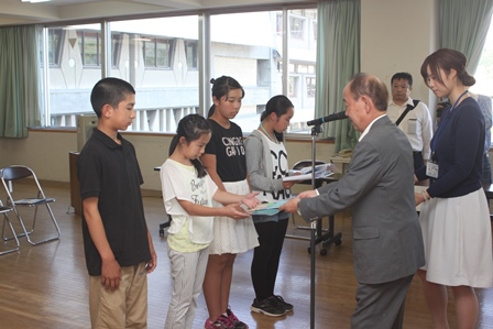 横に並んで立ち、理事長から贈呈品を受け取る四人の児童達の写真