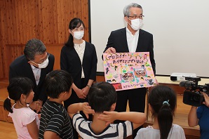 子供たちから手書きの感謝状を受け取っている見せている津秋さん、滝沢さんの写真