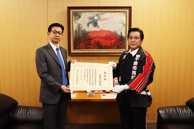 絵画が飾られている室内で副市長と団長が表彰状を手に記念撮影をしている写真