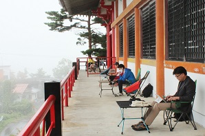見晴らしの良い寺院で簡易椅子に腰かけて作業をする参加者たちの写真