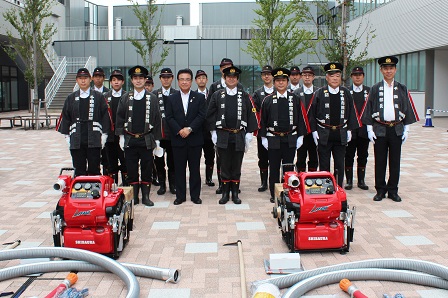 真っ赤な小型ポンプの後ろに並んで記念撮影をしている消防団員の皆さんの写真