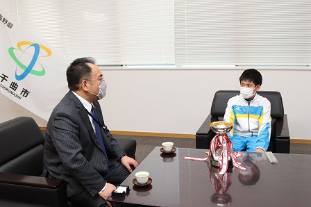 トロフィーが置かれた机を囲むようにして座り、お話している市長と小椋くんの写真