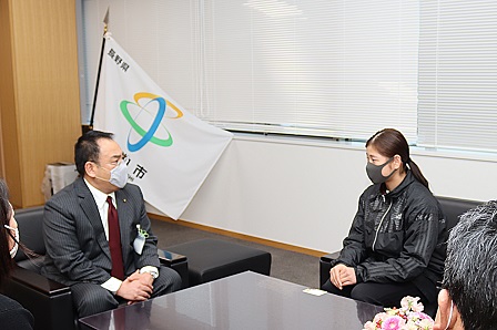 千曲市の旗を背景に、市長室内でお話している笠井さんの写真